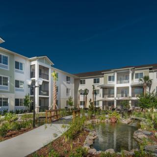 A modern apartment complex with landscaped gardens and a pond.