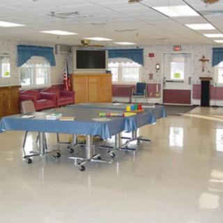 A spacious activity room with tables and chairs, featuring a television and windows.