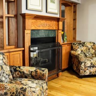 A cozy living room with a wooden fireplace and floral armchairs.