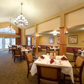 An elegant dining room with neatly arranged tables and chairs, well-lit by chandeliers.