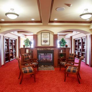 A cozy library with a fireplace, surrounded by bookshelves and a seating area on red carpet.