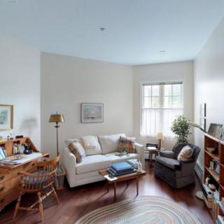 A cozy living room with a sofa, armchair, and bookshelf, featuring a window that lets in natural light.