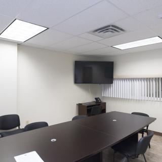 An empty conference room with a large table, chairs, and a wall-mounted television.