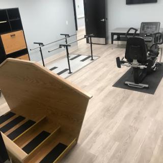 A spacious physical therapy room equipped with stairs, parallel bars, and exercise equipment.