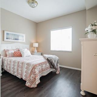 A cozy bedroom featuring a neatly made bed with patterned bedding, a nightstand with a lamp, and a dresser under the window.