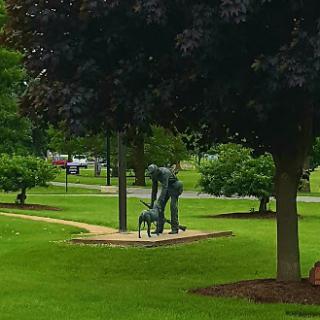 A tranquil park scene featuring a sculpture of a person and a dog, surrounded by lush greenery.