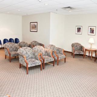 A waiting room with rows of upholstered chairs and framed pictures on the walls.