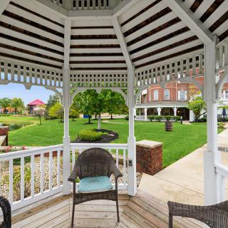 A scenic view from inside a wooden gazebo overlooking a lush garden and brick building.