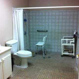 An accessible bathroom with a shower area equipped with a chair and grab bars, suitable for wheelchair users.