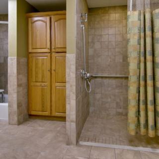 A spacious bathroom with a walk-in shower, wooden cabinet, and tiled walls.
