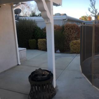 A backyard patio area featuring a fire pit and surrounding bushes.