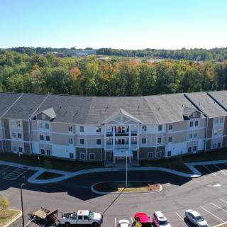 Aerial view of a residential apartment building surrounded by trees in autumn, with a parking lot and several vehicles visible.
