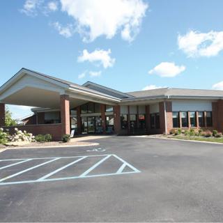 A modern building with a covered entrance and adjacent parking lot under a partly cloudy sky.