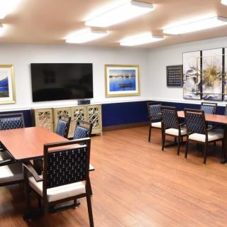 A modern meeting room with tables, chairs, a large television, and wall art.