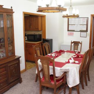 A neatly set dining room with a wooden table and chairs, a chandelier overhead, and a glass-front cabinet in the corner.