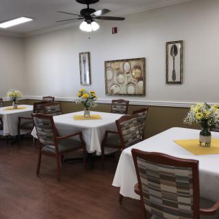 A cozy dining room with neatly arranged tables and chairs, adorned with floral centerpieces and decorative wall art.