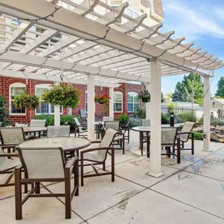 An inviting outdoor patio area with a pergola, featuring tables and chairs surrounded by hanging plants and a brick building background.
