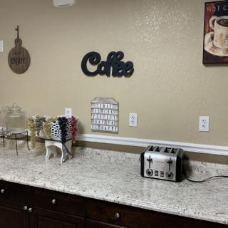 A kitchen countertop featuring a coffee station with cups, a toaster, and decorative wall signs.