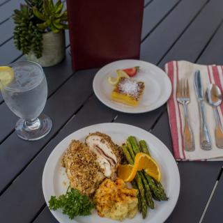 A delicious meal featuring chicken with mashed potatoes and asparagus, accompanied by a dessert and a glass of water with lemon.