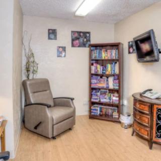 A cozy living room with a recliner chair, bookshelf filled with books, and a wall-mounted television.