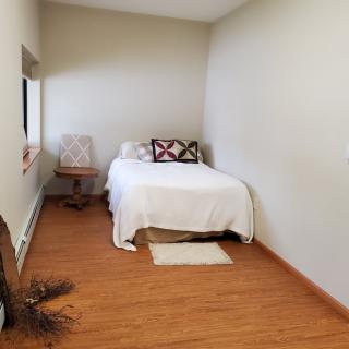 A minimalist bedroom with a single bed, chair, and wooden flooring.