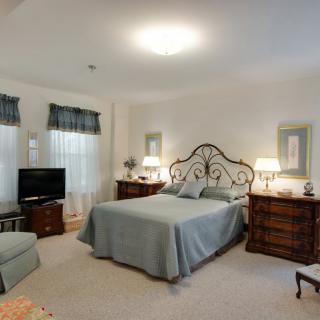 A cozy bedroom with a large bed, two nightstands with lamps, a TV, and a comfortable chair.