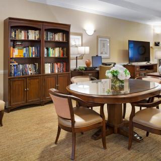 A cozy library room with bookshelves and a round table surrounded by chairs.