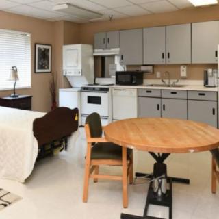 A combined kitchen and bedroom space featuring a dining table, chairs, bed, and kitchen appliances.