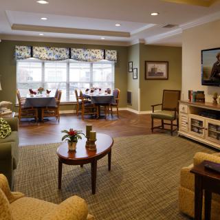 A modern and cozy living room with dining area, featuring elegant furniture, wood flooring, and a large window.