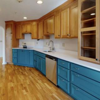 A modern kitchen featuring wooden upper cabinets, blue lower cabinets, and a hardwood floor.