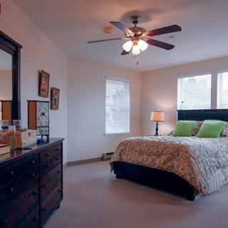 A cozy bedroom featuring a large bed with decorative pillows, a ceiling fan, and a wooden dresser.