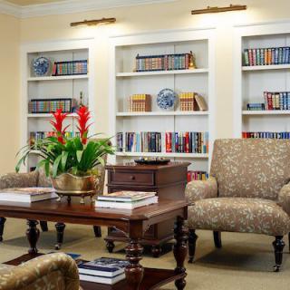 A cozy library room with bookshelves, armchairs, and a coffee table adorned with a vibrant plant.