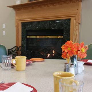 A cozy table setting with mugs and flowers by the fireplace.