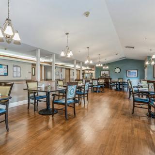 A spacious dining area with elegant lighting and neatly arranged tables on a hardwood floor.