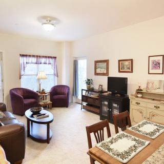 A cozy living room with a small dining area, featuring comfortable seating, a TV, and decorative elements.
