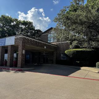 A view of a modern building with a canopy entrance, surrounded by trees and blue sky.