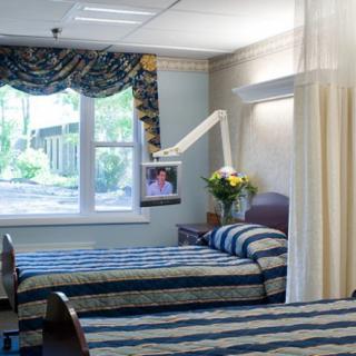 A hospital room with two beds, a television, and a window with curtains.
