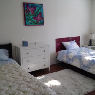 A bright and modern bedroom with two twin beds, a white dresser, and a colorful painting on the wall.