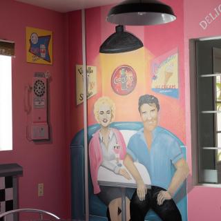 A retro-themed mural inside a diner with pink walls, depicting two people in 1950s attire.