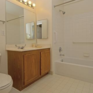 A clean and simple bathroom with a wooden vanity, a large mirror, and a bathtub.