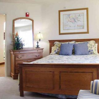 A cozy bedroom featuring a wooden bed, matching dresser with a mirror, and a bedside lamp.