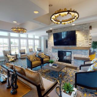 A modern and spacious living room featuring a stone fireplace, large TV, and stylish furnishings.