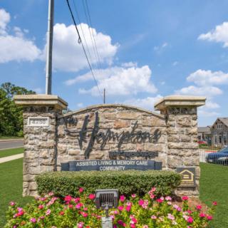 Entrance sign to a community with flowers and a stone structure on a sunny day.