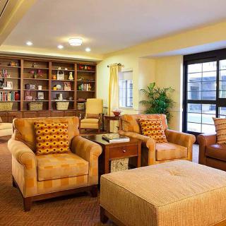A cozy living room with comfortable armchairs and bookshelves, illuminated by bright lighting.