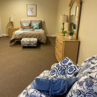 A cozy bedroom featuring a bed with patterned cushions, a dresser with a mirror, and warm lighting.
