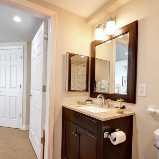 A neatly designed bathroom with a dark wood vanity, featuring a large mirror and overhead lighting.
