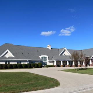 A large residential house with a driveway and well-maintained lawn under a clear blue sky.