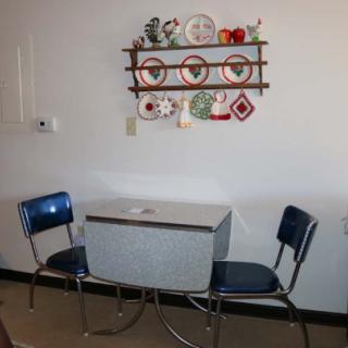 A cozy retro kitchen nook with a small table, vintage chairs, and decorative wall shelves.