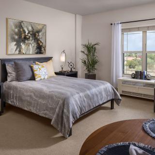 A modern bedroom with stylish decor, featuring a large bed, artwork, and a window with natural light.
