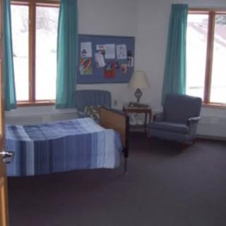 A simple bedroom with a bed, chair, and a bulletin board near the window.